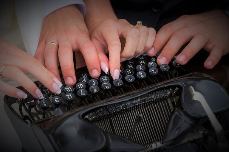 foto di quattro mani di una coppia di sposi che scrivono assieme su una macchina da scrivere